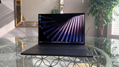 Black Dell XPS 14 2026 laptop on glass table in front of a mirror on a wall and green plants in the background.