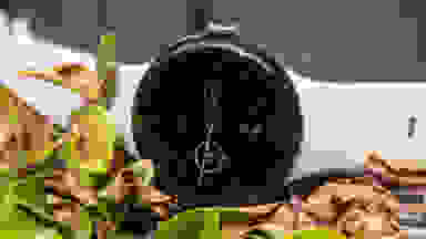 The Google Pixel Watch 2, with a white band and black face, sits in a pile of leaves.
