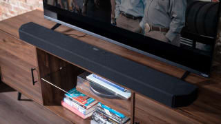 A black soundbar sits on a walnut coloured stand below a black TV and above some blu-rays.