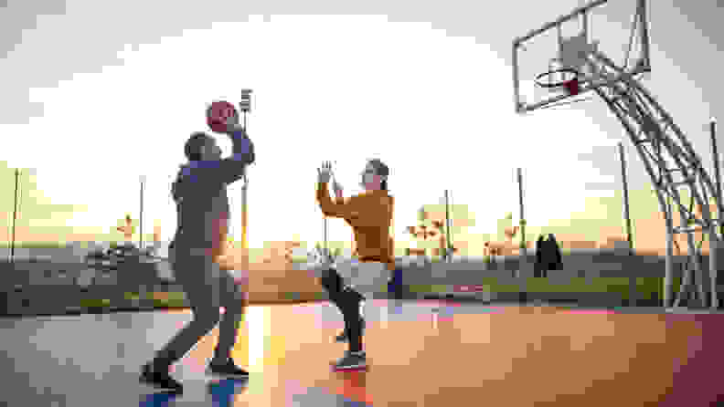Two people playing basketball on an outside court.