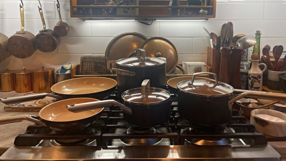 Assorted two-toned Ninja pots and pans on top of range in front of tile wall in kitchen next to utensils.