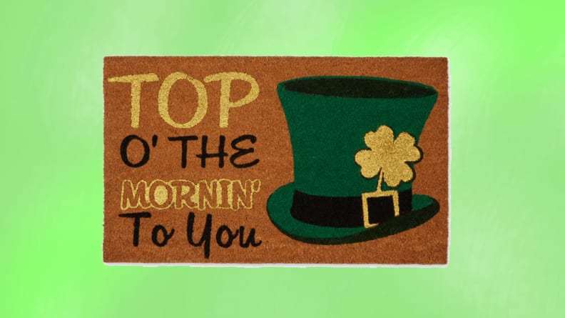 A brown doormat with Top Of The Mornin' To You with a green tophat in front of a green background.
