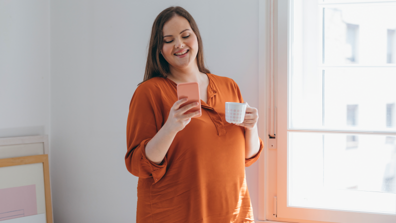 A woman drinking coffee and smiling while looking at her phone