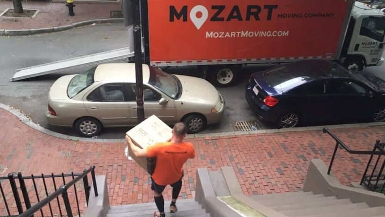 A mover going down the stairs carrying a box to load inside a  moving truck