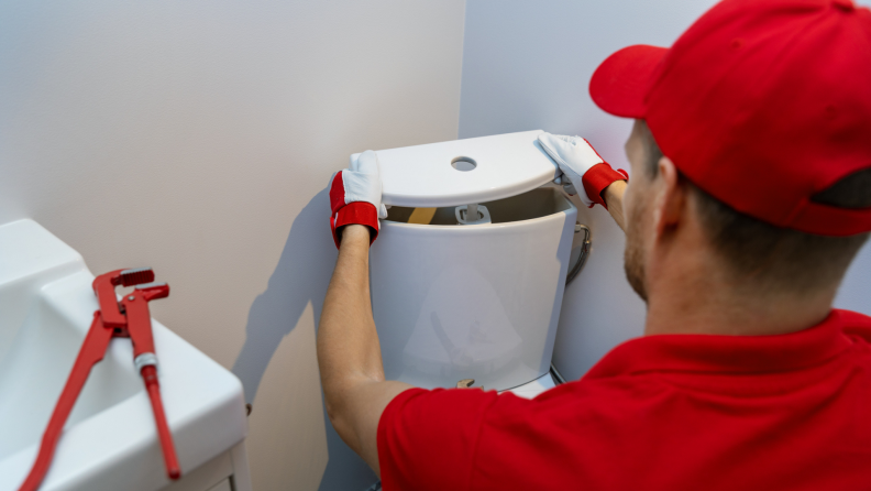 Plumber in red hat and red polo lifting up lid of toilet