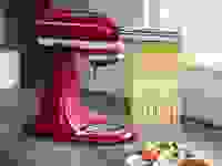 红色的KitchenAid搅拌机与KitchenAid意大利面附件举行意大利扁面在柜台上