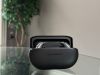 An open black charging case with hearing aids inside sits on top of a glass table with a tree in the background
