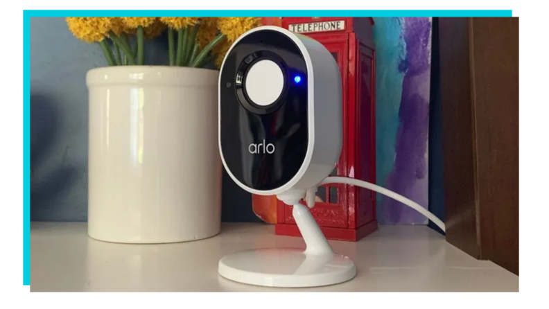 Arlo indoor security camera on table next to pot of flowers.