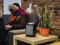 A woman sits on a couch in a cold room wrapped in a jacket.