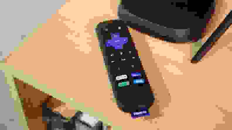 streaming remote lying next to small black streaming box on a wooden table.