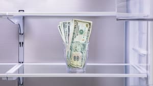 A glass with cash in it sitting on an empty refrigerator shelf.