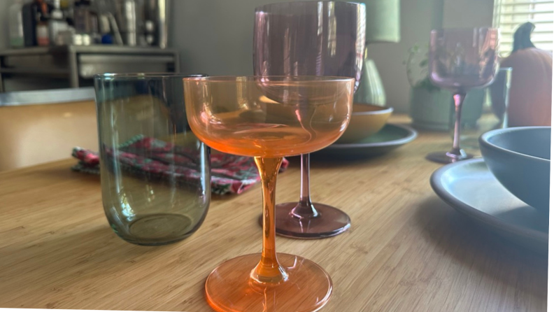 An orange coupe, purple wine glass, and green tumbler on a dining room table.