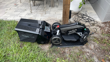 EcoFlow Blade Robotic Lawn Mower outdoors on grassy lawn next to patio.