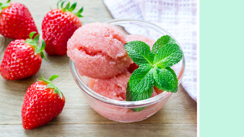 Close up of a cup of strawberry sorbet surrounded by strawberries.