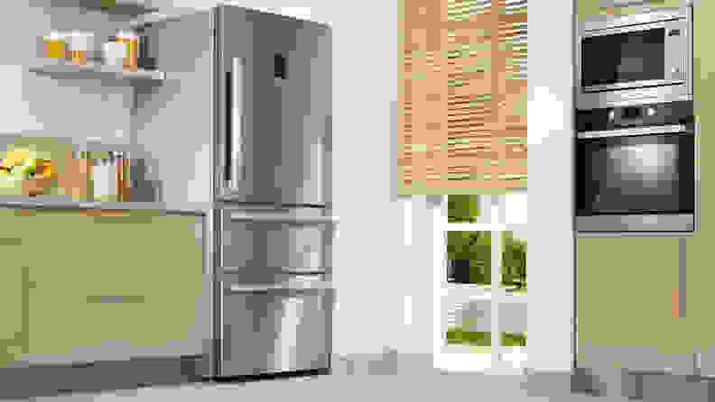 A stainless steel refrigerator unit in a kitchen with light hardwood cabinets, a microwave and an oven.