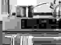Close-up of a stainless steel induction range. A metallic pot and tea kettle sit atop the range.