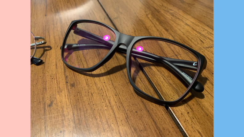 A pair of glasses on a tabletop. The light reflected in the lenses is purple.
