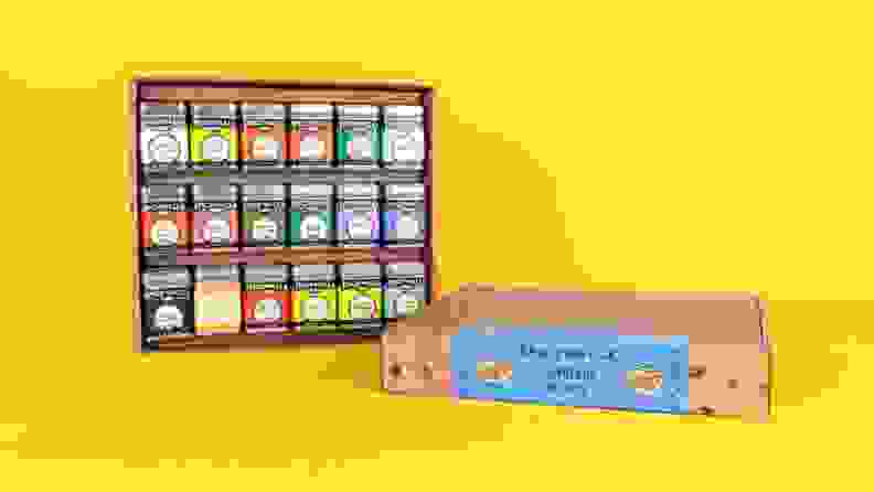 An assortment of spice tins arranged in a cardboard box against a bright yellow background.