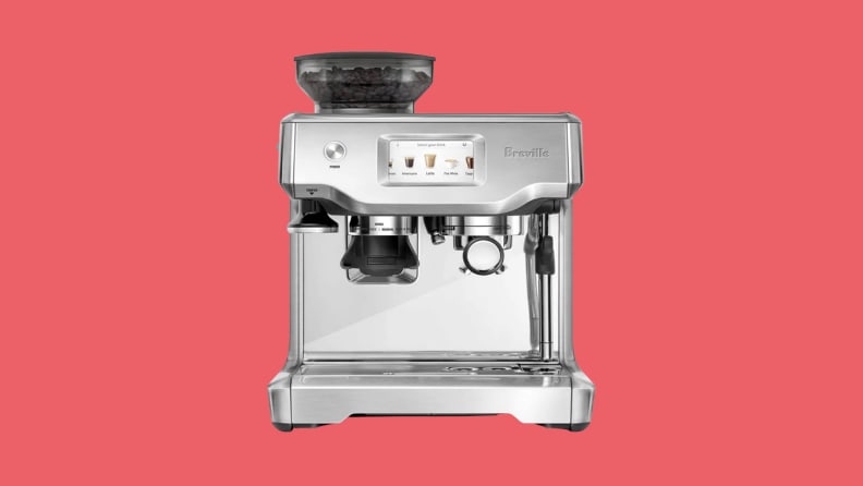 stainless steel espresso machine: Breville Barista Touch on a white countertop with surrounding accessories.