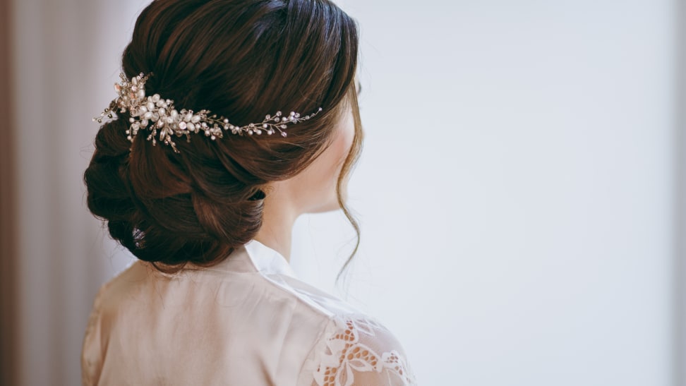 Person displays bridal hair with accessory in bun.