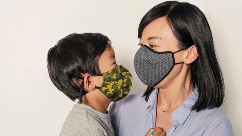 A parent wears a mask while holding their masked child.