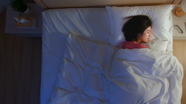 女人安静地睡在床上，旁边的眼镜和床头灯。