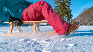Girls slides across a frozen lake on a sled wearing snow pants.