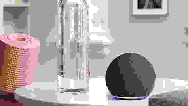 The Amazon Echo Dot 4th generation on a white side table besides a bottle of water.