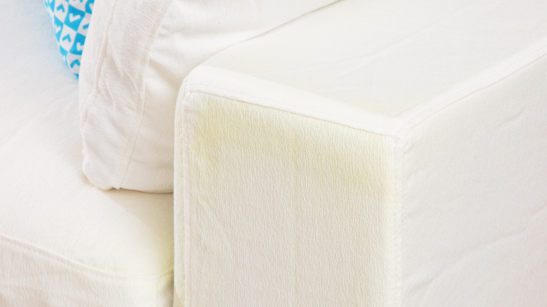 A close-up of the arm of the sofa with some yellow discoloration on the white fabric.