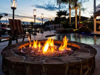 A fire pit lit up in a house's backyard next to a pool.
