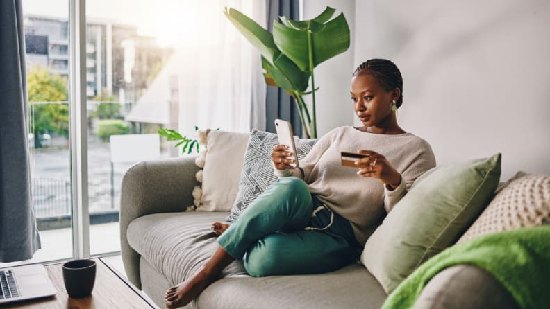Person looking at smart phone and credit while sitting on couch.