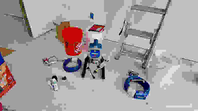 A Graco Magnum X5 Airless Paint Sprayer next to an orange and white bucket in a room under construction.