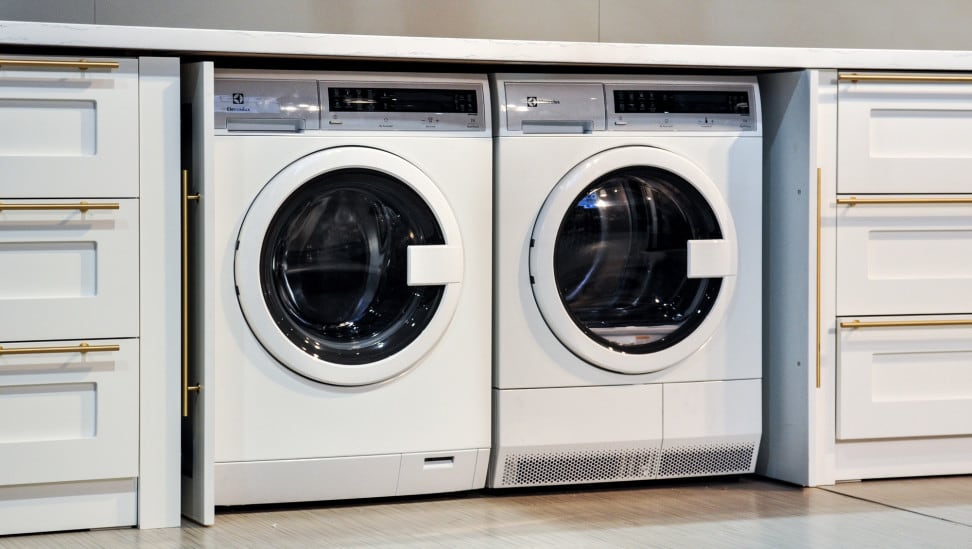 A compact washer and dryer underneath a countertop, in a cutout in the surrounding cabinetry.