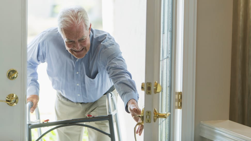 An elderly person utilizing a walker opens a house door.