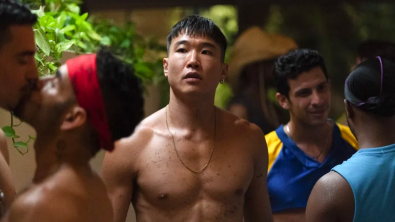 A still from the film 'Fire Island' featuring Joel Kim Booster as Noah standing in a crowded space.