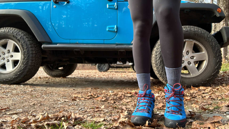 Close-up of someone wearing blue hiking boots next to a blue Jeep.