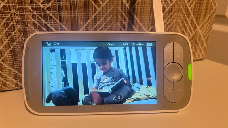 Small child reading a book inside of crib on the screen of the Infant Optics DXR-8 Pro baby monitor.