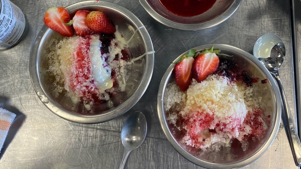 Two bowls of shaved ice with assorted colorful toppings sitting on top of a stainless steel surface.