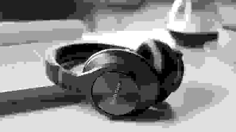 A pair of shiny, charcoal-colored over-ear headphones sit next to a computer on a modern desk.