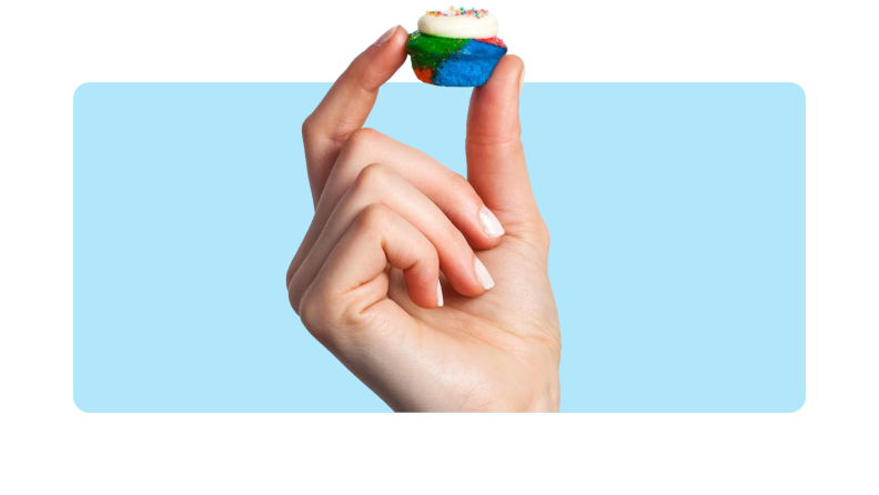 A hand holding up a mini cupcake in front of a background.