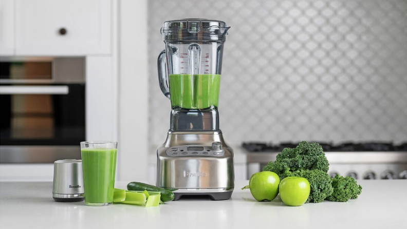 The Breville blender is displayed next to a glass of healthy green juice, celery, green apples, and other ingredients.