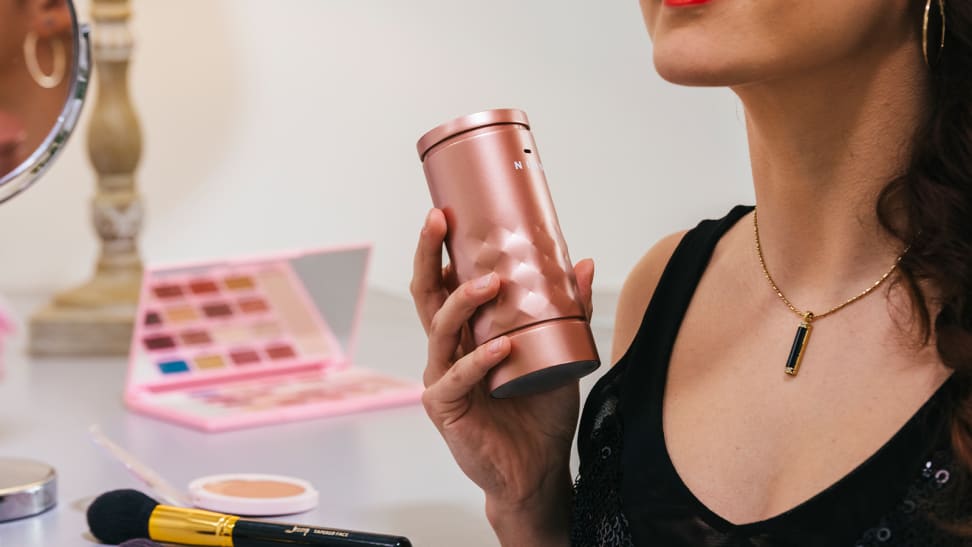 A person holding up a rose gold canister of perfume.