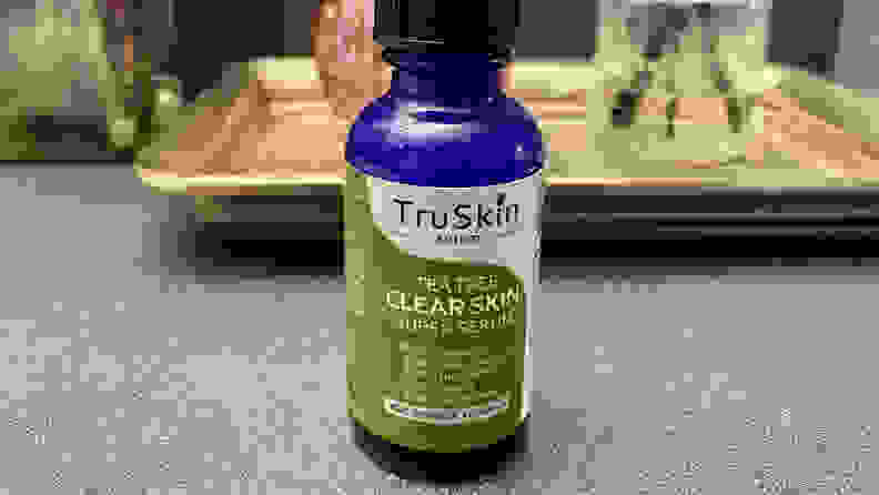 A blue bottle of TruSkin serum sits on a countertop. The label is marked with some of its contents: twenty percent vitamin C, five percent hyaluronic acid, and so on.