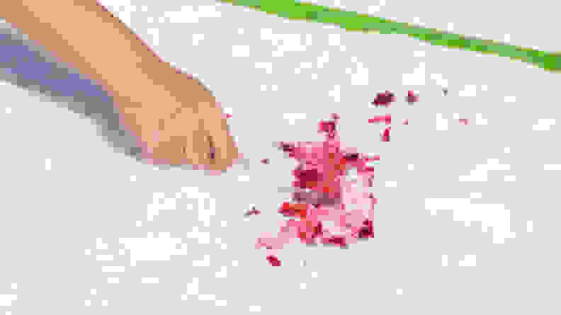 A person's hand spreads red cranberry sauce with a spoon on a white shag rug