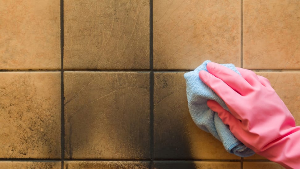 Hand with pink glove wiping down soot on a tile wall with a microfiber towel