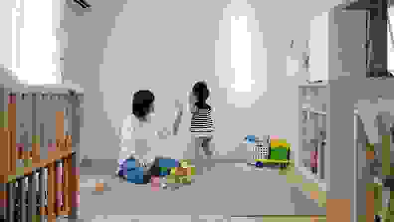 A mother and child play with building blocks in a tidy, well-lit playroom.