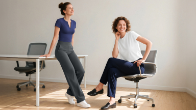 Two women in an office setting smile while modeling comfortable, professional G4free pants.