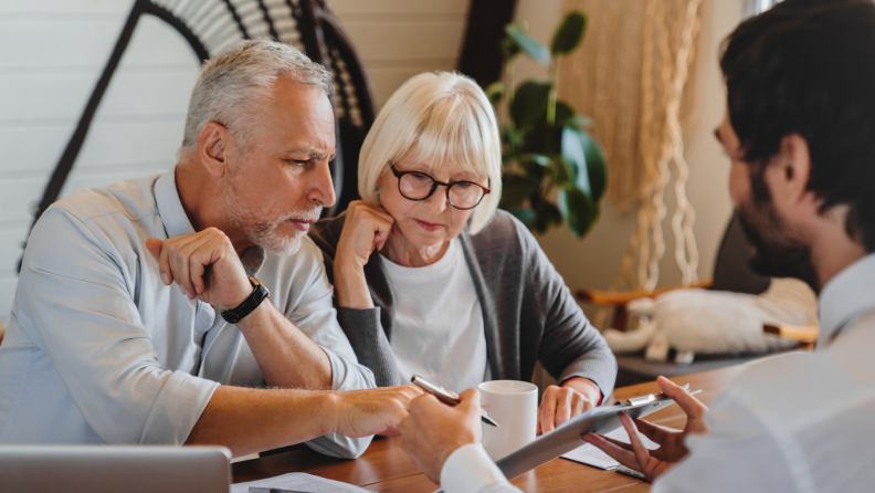 Two older people sitting at table having a conversation with specialist.