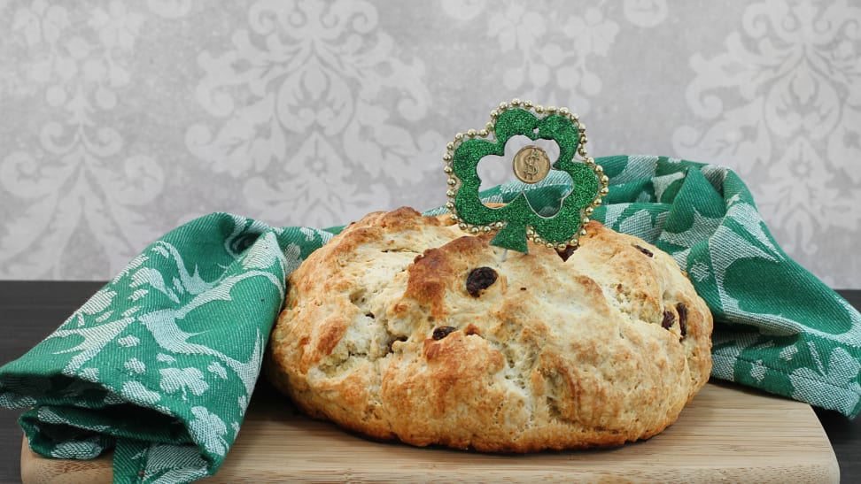 An Irish soda bread is sitting on a cutting board covered with Irish St-Patricks-Day-themed decorations