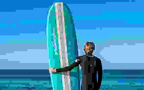 A guy taking his board into the ocean to surf.